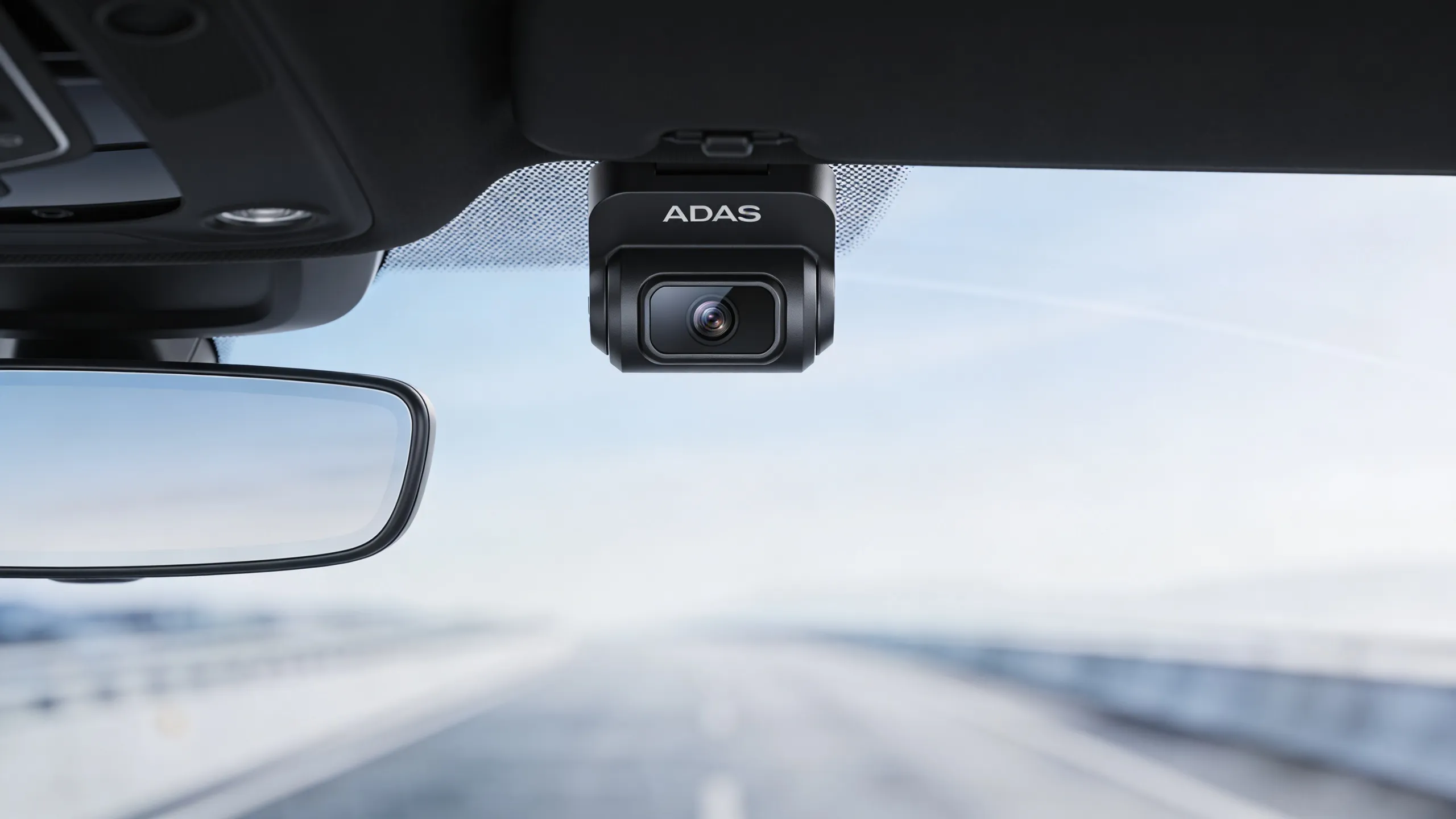 Close-up of forward-facing ADAS camera mounted behind rearview mirror on vehicle windshield showing camera housing detail
